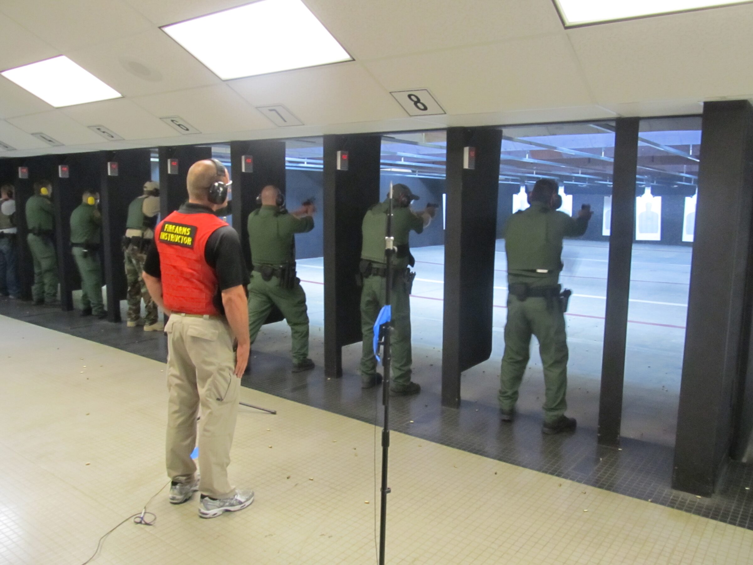 Certified firearms instructor supervising live-fire handgun training at an indoor range